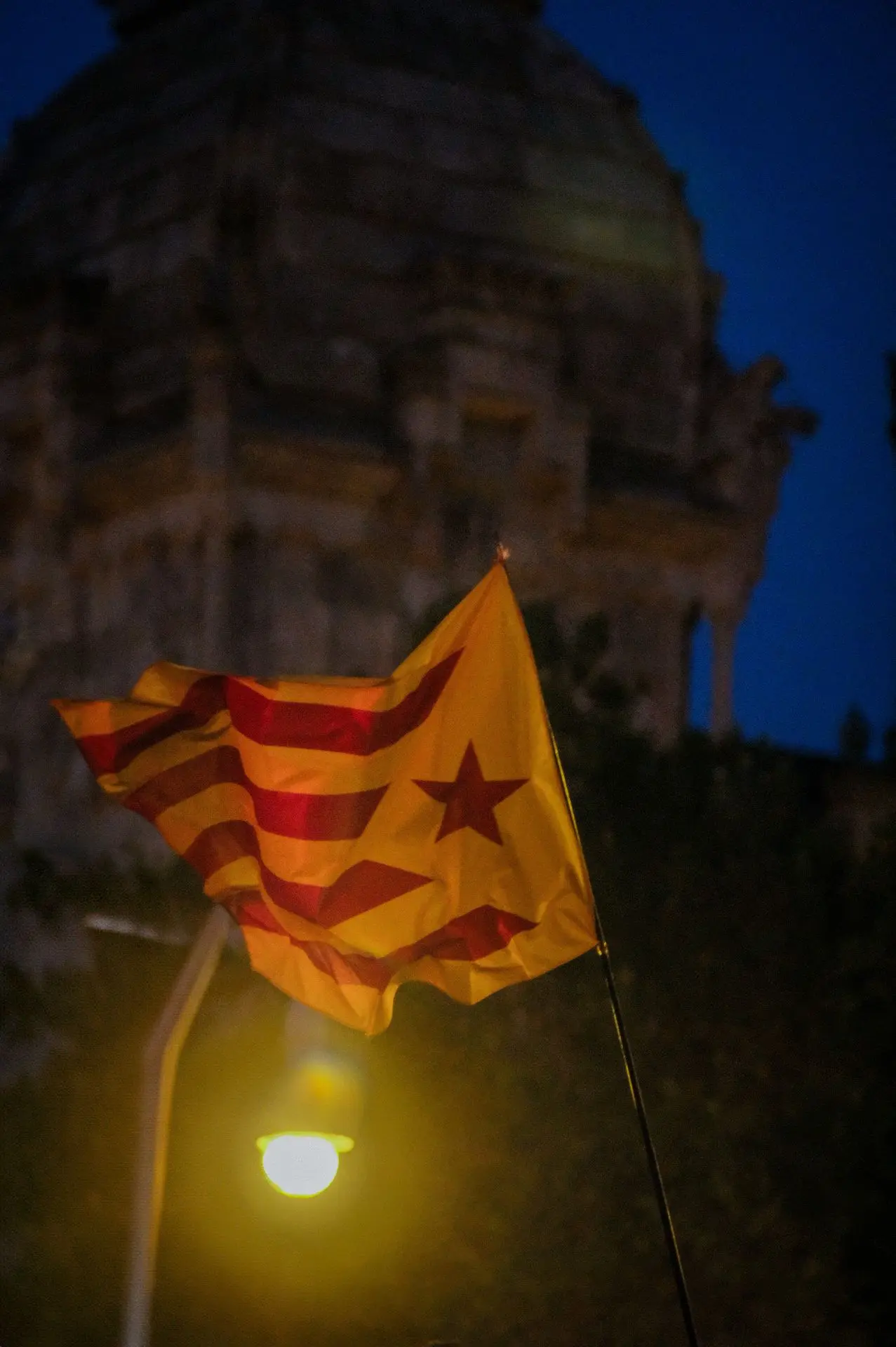 This image is a powerful visual statement of identity and resistance. The estelada, the Catalan independence flag, waves dynamically, symbolizing a movement that is both deeply rooted in history and continuously evolving. The absence of the person holding it adds a layer of universality—this flag represents not just an individual but an entire collective, a sentiment that transcends a single moment. The interplay of light and movement gives the fabric a sculptural quality, emphasizing the fluidity of political and cultural expression in Barcelona’s ever-changing landscape.